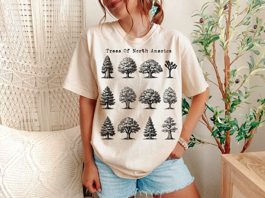 Person wearing a white t-shirt with tree illustrations and text, standing in a room with plants.