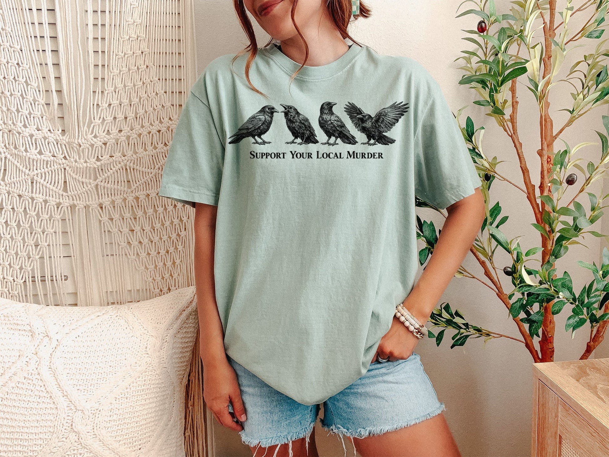 A Bay Unisex Garment-Dyed T-shirt mockup (front view) showing the support your local murder crow shirt - funny bird lover gift - dark academia raven tee print on the front. The artwork highlights goth aesthetic, crow lover gift, witchy clothing, cottagecore shirt, funny crow pun, support your local murder crow shirt - funny bird lover gift - dark academia raven tee, unisex garment-dyed t-shirt, bay, support, your, describing the graphic and theme on the garment.