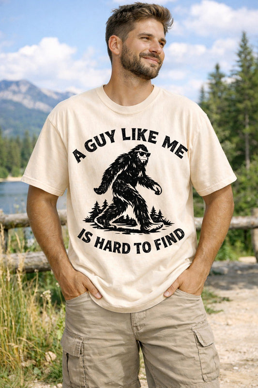 A Ivory Unisex Garment-Dyed T-shirt mockup (front view) showing the funny bigfoot shirt for men - a guy like me is hard to find t-shirt print on the front. The artwork highlights gift for him, rare breed shirt, funny guy gift, boyfriend birthday, sarcastic mens tee, bigfoot lover gift, hard to find guy, cryptid apparel, outdoor humor shirt, funny dad gift, describing the graphic and theme on the garment.