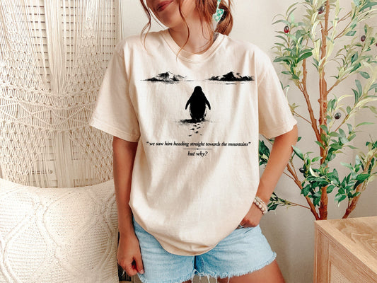 A Ivory Unisex Garment-Dyed T-shirt mockup (front view) showing the funny absurdist penguin t-shirt - nothing matters dark humor gift print on the front. The artwork highlights existential dread, dark humor shirt, absurdist art, funny penguin tee, nothing matters, antarctic meme, goth penguin, gift for nihilist, quiet quitting, burnout shirt, describing the graphic and theme on the garment.