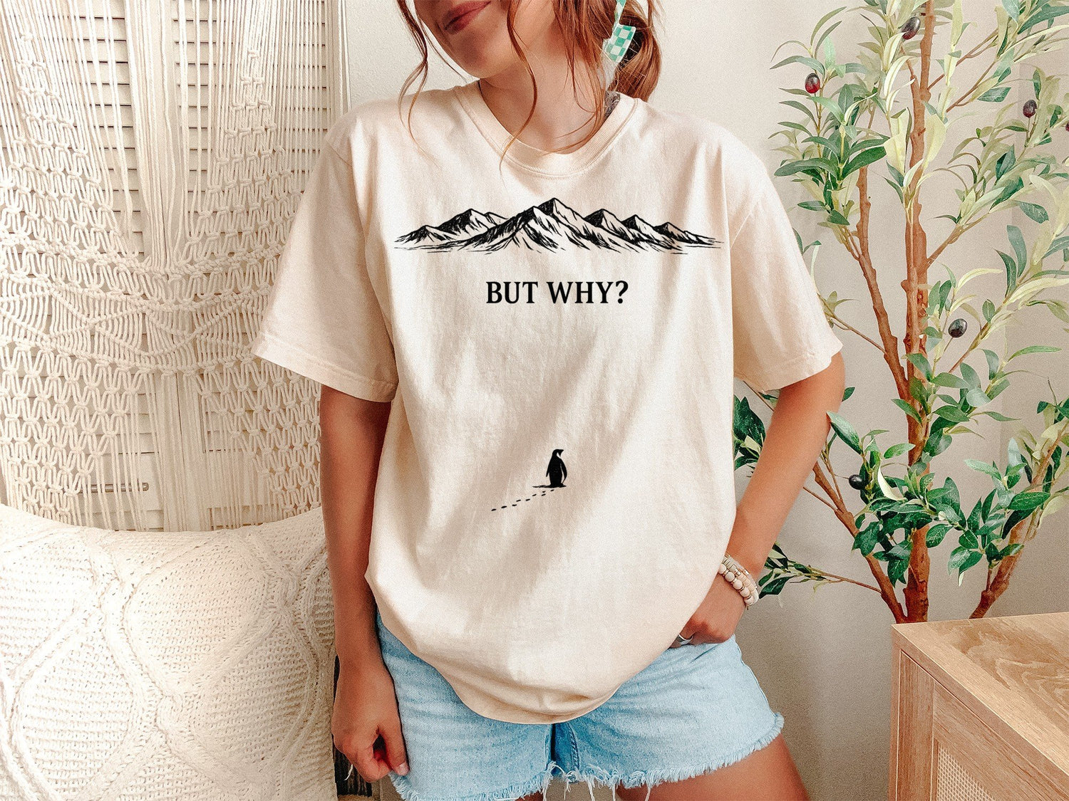 A Ivory Unisex Garment-Dyed T-shirt mockup (front view) showing the funny depressed penguin meme tee - lone penguin mountain journey print on the front. The artwork highlights nihilist penguin, existential humor, werner herzog, funny animal tee, minimalist graphic, meme clothing, unhinged shirt, burnout gift, indie film merch, penguin lover gift, describing the graphic and theme on the garment.