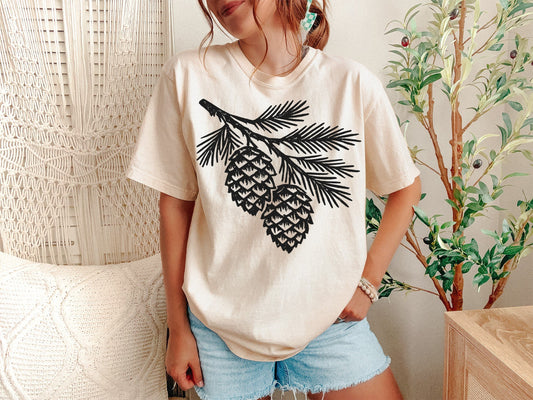 A Ivory Unisex Garment-Dyed T-shirt mockup (front view) showing the vintage pine tree t-shirt - forest graphic tee - granola girl aesthetic print on the front. The artwork highlights minimalist tee, hiking shirt, camping apparel, forest graphic tee, granola girl, gorpcore aesthetic, vintage nature shirt, evergreen tree tee, outdoor adventure, comfort colors shirt, describing the graphic and theme on the garment.