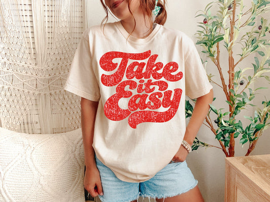 A Ivory Unisex Garment-Dyed T-shirt mockup (front view) showing the take it easy retro typography shirt 90s aesthetic graphic tee print on the front. The artwork highlights 70s graphic shirt, comfort colors tee, oversized aesthetic, skeleton shirt, western boho tee, positive quote shirt, slow living style, vintage 70s shirt, smiley face tee, wavy text shirt, describing the graphic and theme on the garment.