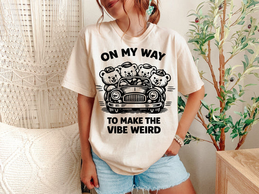 A Ivory Unisex Garment-Dyed T-shirt mockup (front view) showing the on my way to make my vibe weird shirt - funny raccoon meme tee print on the front. The artwork highlights trash panda tee, funny raccoon gift, social anxiety shirt, neurospicy shirt, weirdcore aesthetic, unhinged graphic tee, sarcastic animal, introvert humor, retro meme shirt, making it weird, describing the graphic and theme on the garment.