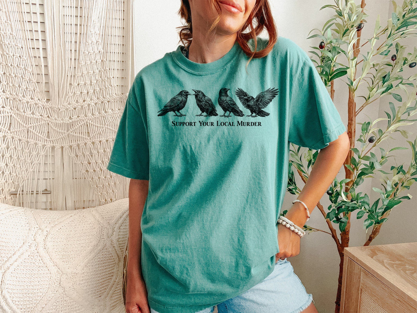 A Light Green Unisex Garment-Dyed T-shirt mockup (front view) showing the support your local murder crow shirt - funny bird lover gift - dark academia raven tee print on the front. The artwork highlights goblincore, dark academia, raven shirt, bird watcher gift, goth aesthetic, crow lover gift, witchy clothing, cottagecore shirt, funny crow pun, support your local murder crow shirt - funny bird lover gift - dark academia raven tee, describing the graphic and theme on the garment.