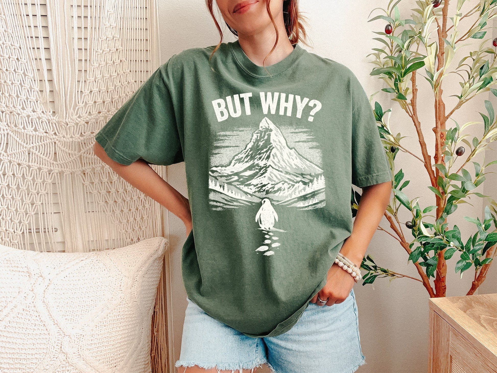 A Moss Unisex Garment-Dyed T-shirt mockup (front view) showing the but why be the damn penguin shirt - sarcastic existential top print on the front. The artwork highlights nihilist penguin, existential humor, werner herzog, funny animal tee, minimalist graphic, meme clothing, unhinged shirt, burnout gift, indie film merch, penguin lover gift, describing the graphic and theme on the garment.