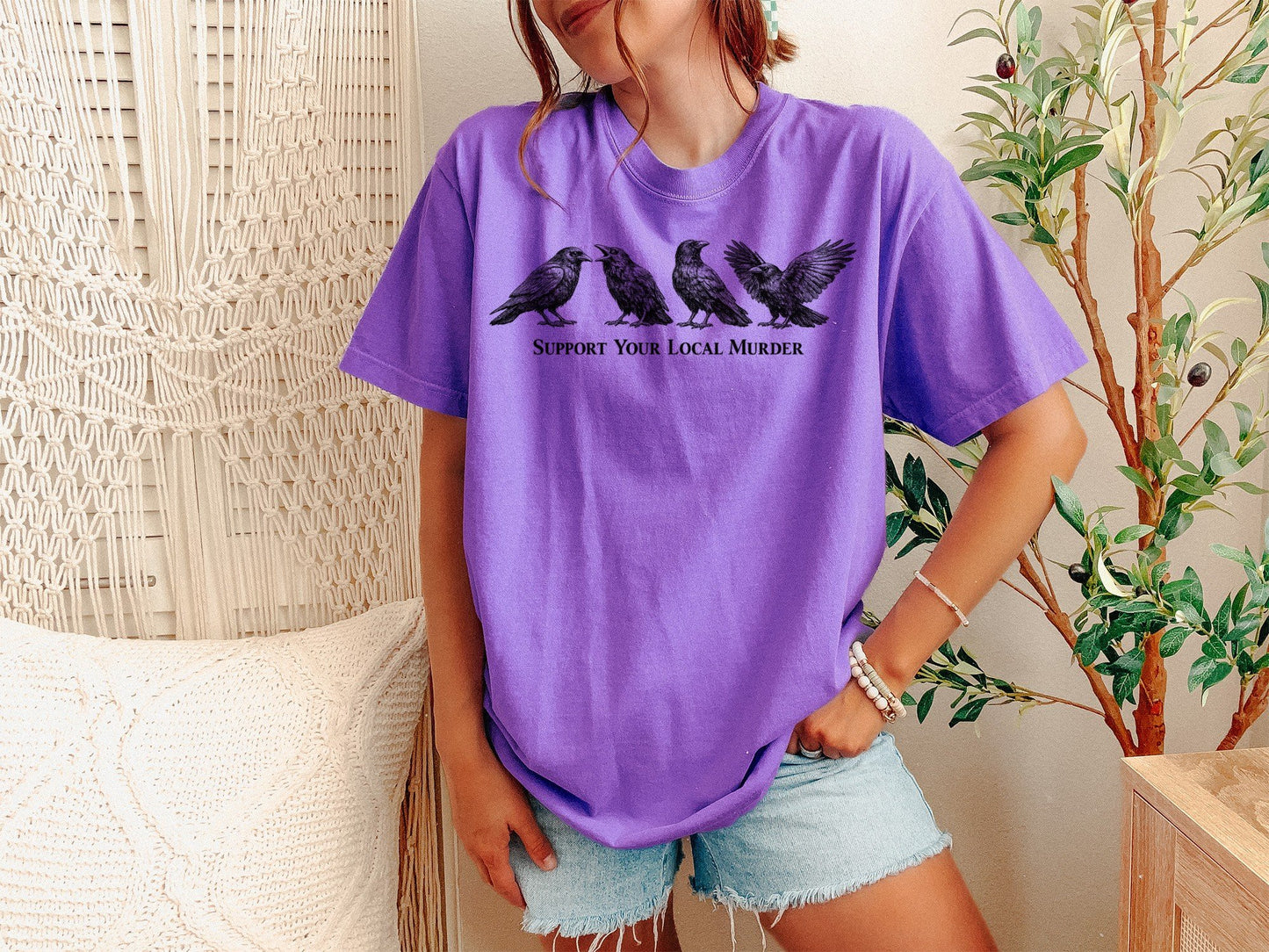 A Violet Unisex Garment-Dyed T-shirt mockup (front view) showing the support your local murder crow shirt - funny bird lover gift - dark academia raven tee print on the front. The artwork highlights unisex garment-dyed t-shirt, violet, support, your, local, murder, crow, shirt, -, funny, describing the graphic and theme on the garment.