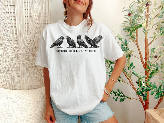 A White Unisex Garment-Dyed T-shirt mockup (front view) showing the support your local murder crow shirt - funny bird lover gift - dark academia raven tee print on the front. The artwork highlights funny crow pun, support your local murder crow shirt - funny bird lover gift - dark academia raven tee, unisex garment-dyed t-shirt, white, support, your, local, murder, crow, shirt, describing the graphic and theme on the garment.