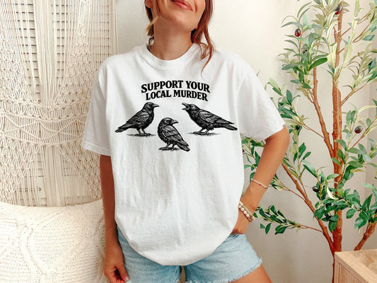 A White Unisex Garment-Dyed T-shirt mockup (front view) showing the support your local murder shirt - vintage crow graphic tee - dark academia aesthetic print on the front. The artwork highlights vintage crow tee, support your local murder shirt - vintage crow graphic tee - dark academia aesthetic, unisex garment-dyed t-shirt, white, support, your, local, murder, shirt, -, describing the graphic and theme on the garment.